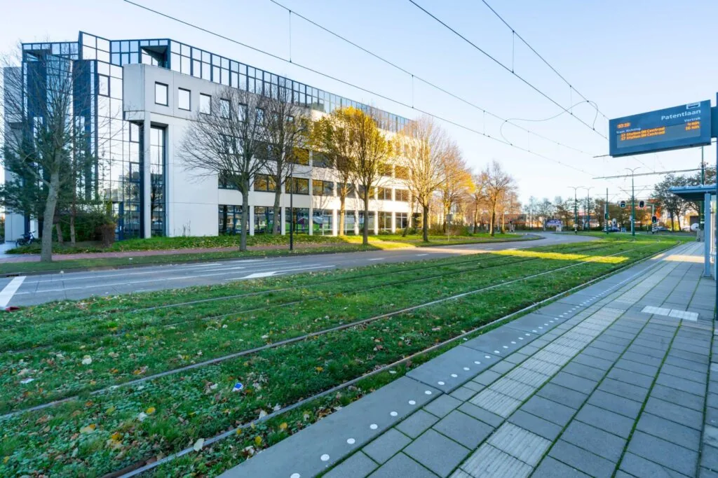 Tramhalte aan de De Bruyn Kopsstraat met zicht op een modern kantoorgebouw en herfstbomen.